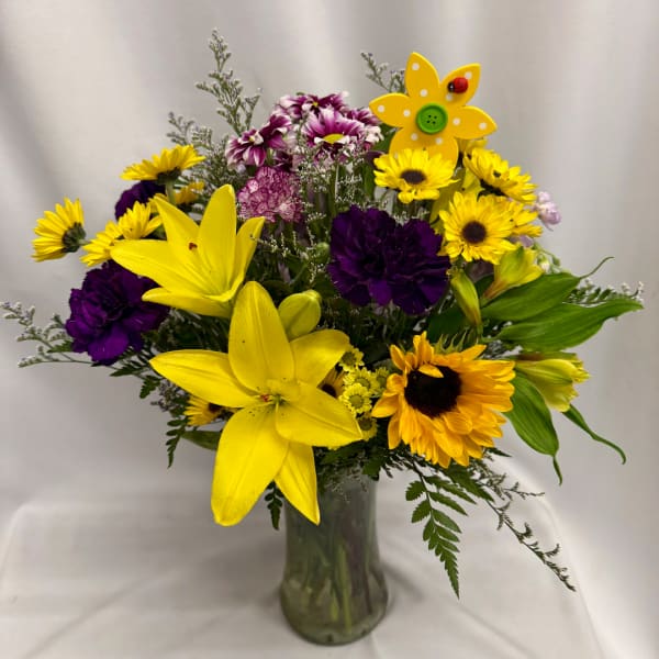 Bouquet of yellow lilies, sunflowers, and purple flowers in a glass vase