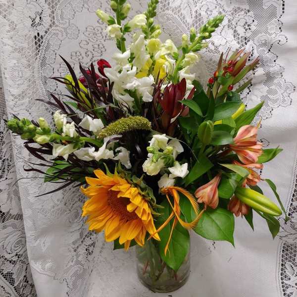Mixed bouquet with sunflowers, white snapdragons, and lilies in a glass vase