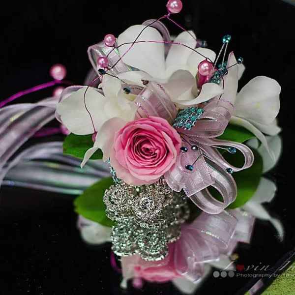 Pink rose corsage with white orchids and ribbon on a black box