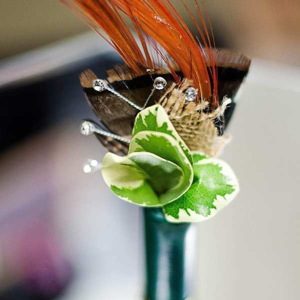 Decorative boutonniere with orange feathers and green variegated leaves