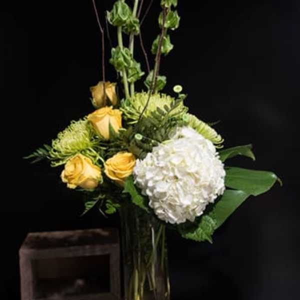 Yellow roses and a white hydrangea in a tall glass vase