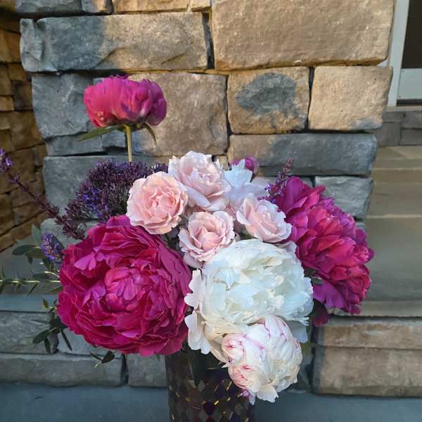 Pink and white peonies with small roses in a dark vase