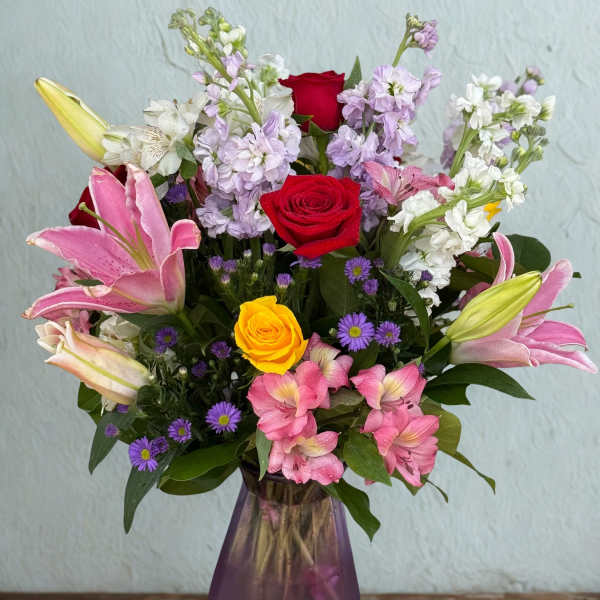 Mixed bouquet of roses, lilies, and purple flowers in a purple vase