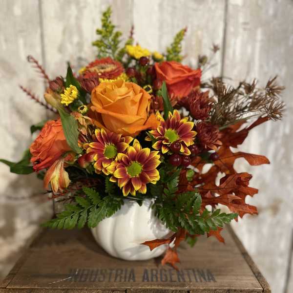 Autumn bouquet with orange roses and yellow-red chrysanthemums in a white pumpkin vase