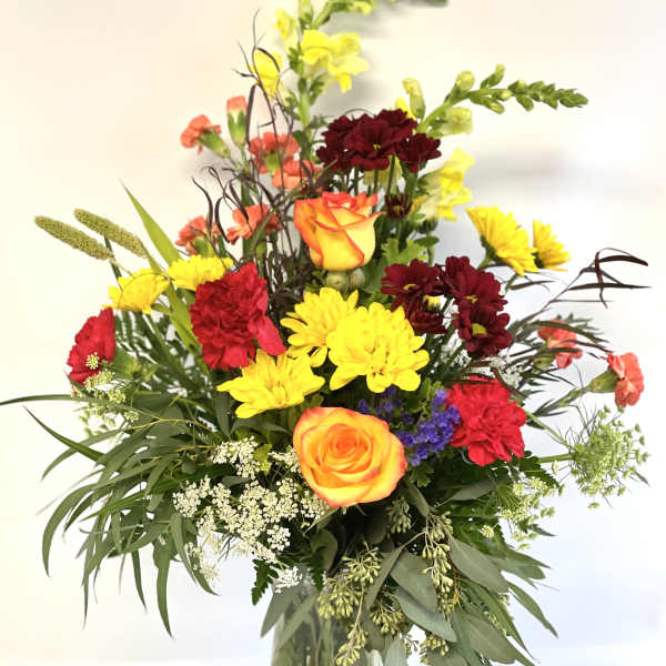 Mixed bouquet of roses, carnations, and yellow blooms in a glass vase