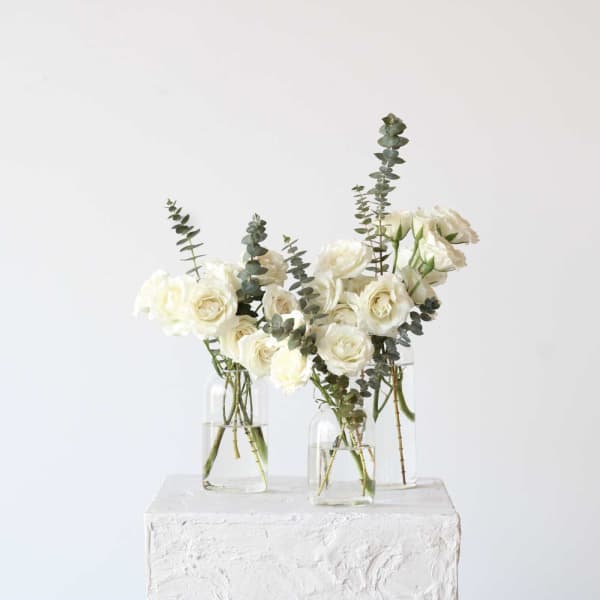 White roses in clear glass vases with tall eucalyptus stems