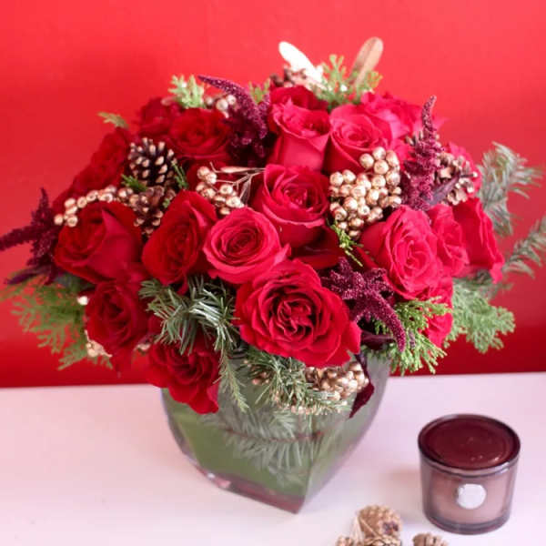 Red rose arrangement in a glass vase with pinecones and berries