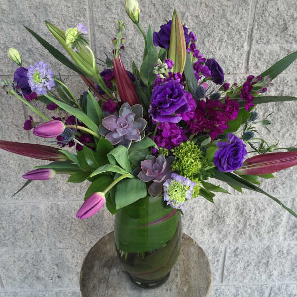 Purple floral arrangement in a glass vase with tulips and succulents