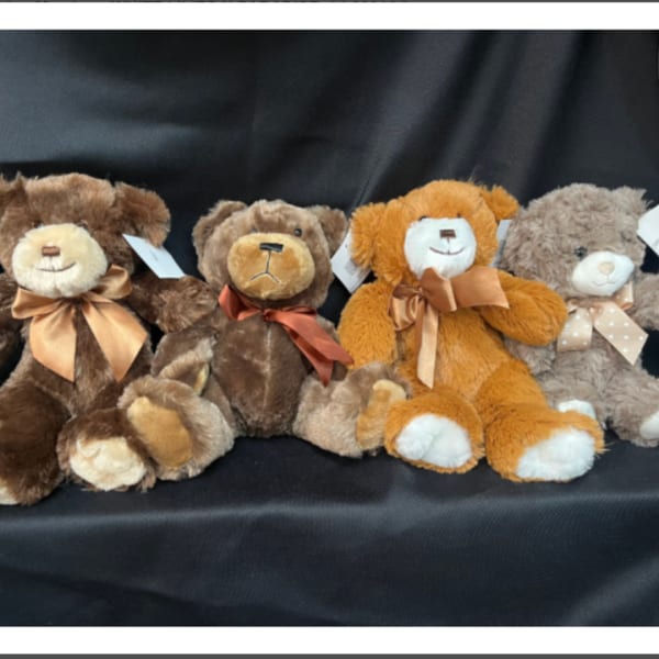 Four plush teddy bears with ribbon bows on a black fabric background