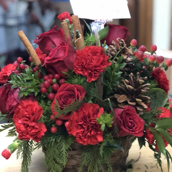 Red roses and carnations arranged in a basket with pinecones and berries