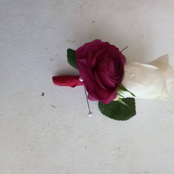 Magenta rose boutonniere with white ribbon and green leaves