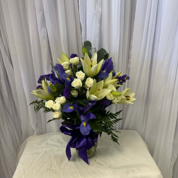 Bouquet of white lilies, white roses, and purple irises in a glass vase
