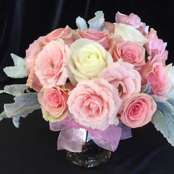 Pink and white rose bouquet in a glass vase with a purple ribbon