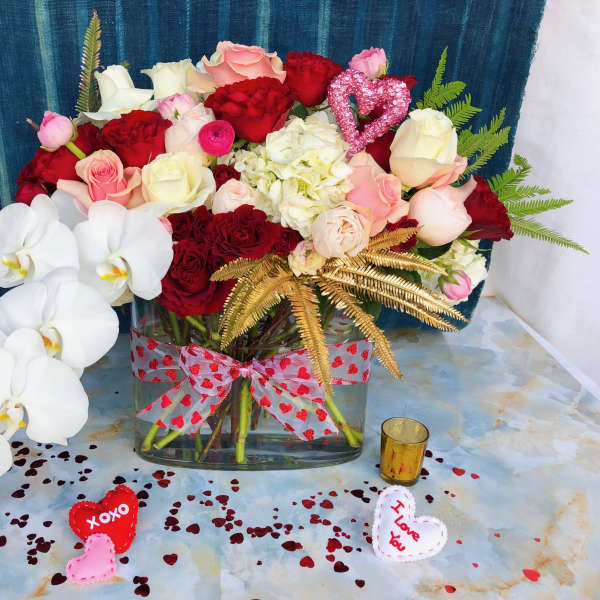 Mixed roses and orchids in a glass vase with heart decorations