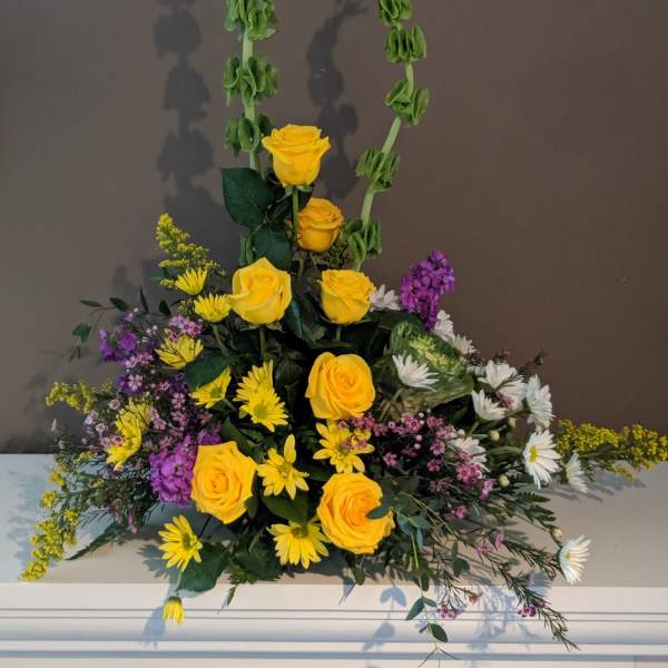 Tall floral arrangement with yellow roses, daisies, and purple accents