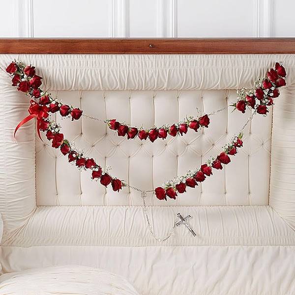 Red rose garlands draped across a white tufted headboard with a small cross pendant