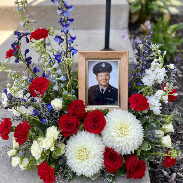 Memorial floral arrangement with a framed portrait, red roses, white blooms, and blue flowers