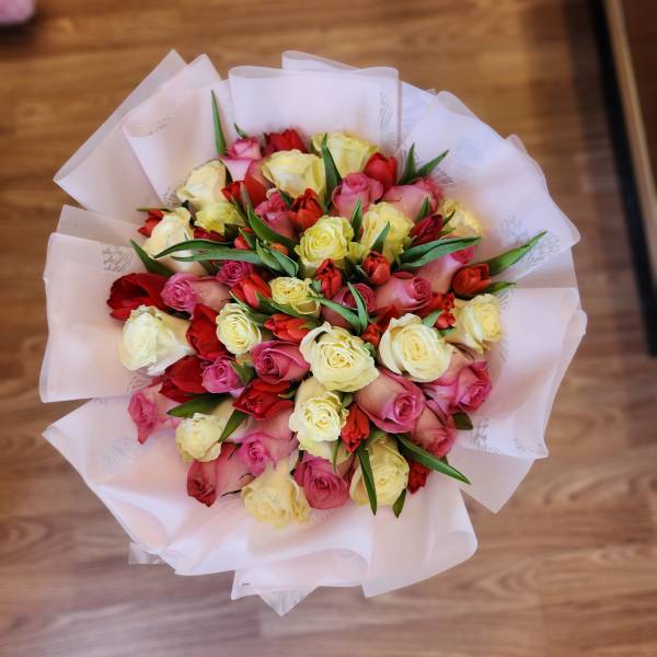 Bouquet of pink, red, and yellow roses wrapped in white paper
