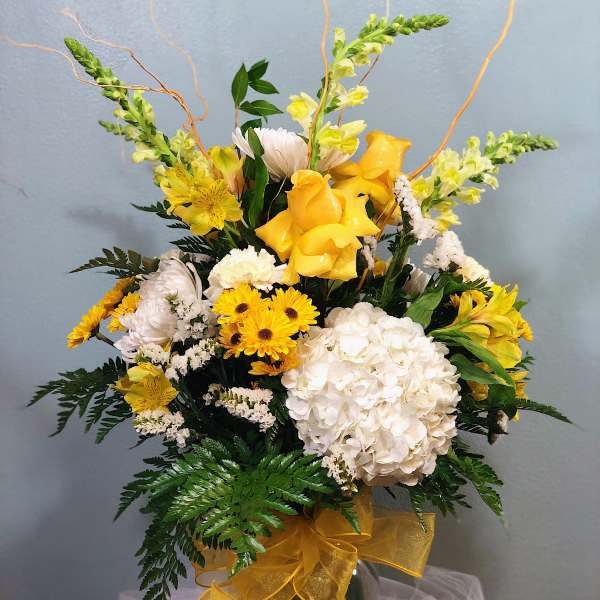 Yellow and white floral arrangement in a glass vase with ribbon