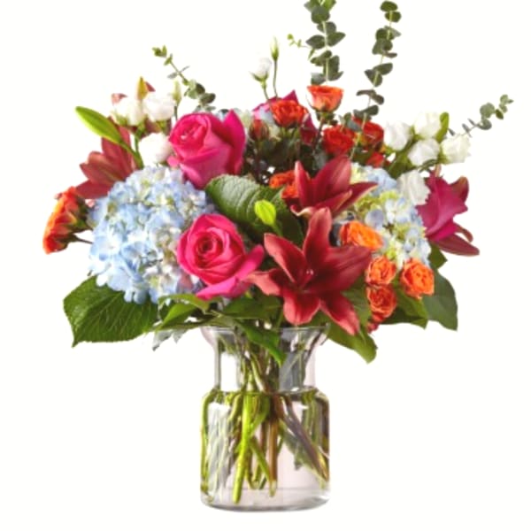 Mixed bouquet of pink roses, lilies, and blue hydrangeas in a glass vase