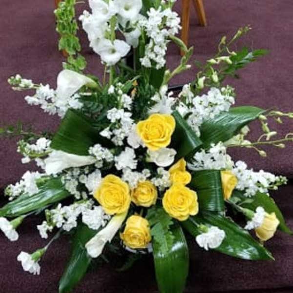 White and yellow floral arrangement with tall stems and broad leaves