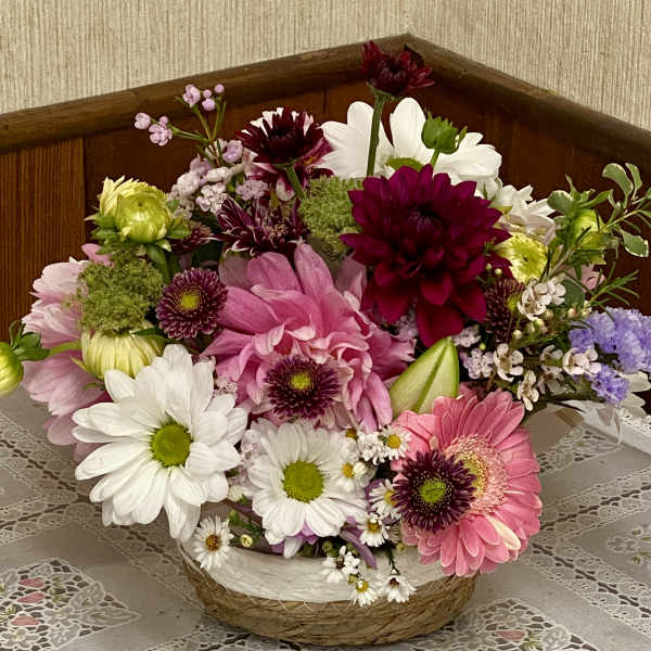 Mixed bouquet of pink, white, and burgundy flowers in a woven basket