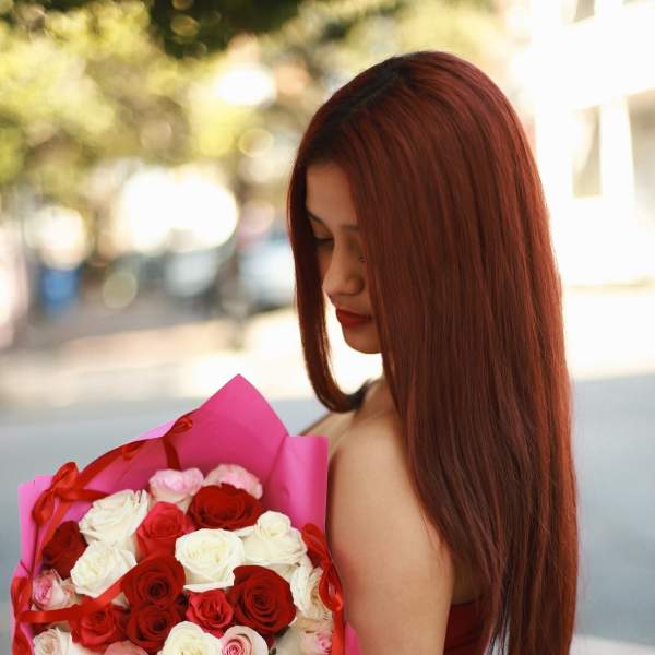 Woman holding a bouquet of red, white, and pink roses wrapped in pink paper