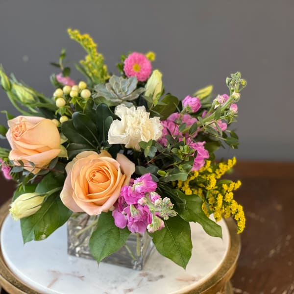 Peach roses and pink flowers in a square glass vase