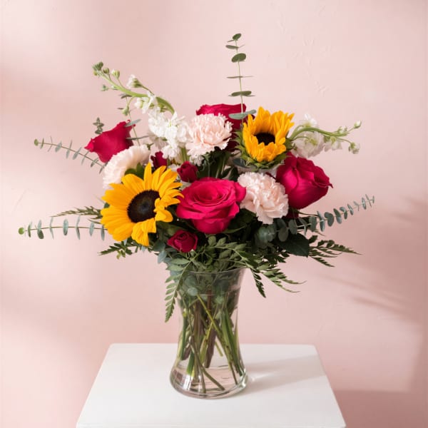 Bouquet of roses, sunflowers, and carnations in a clear glass vase
