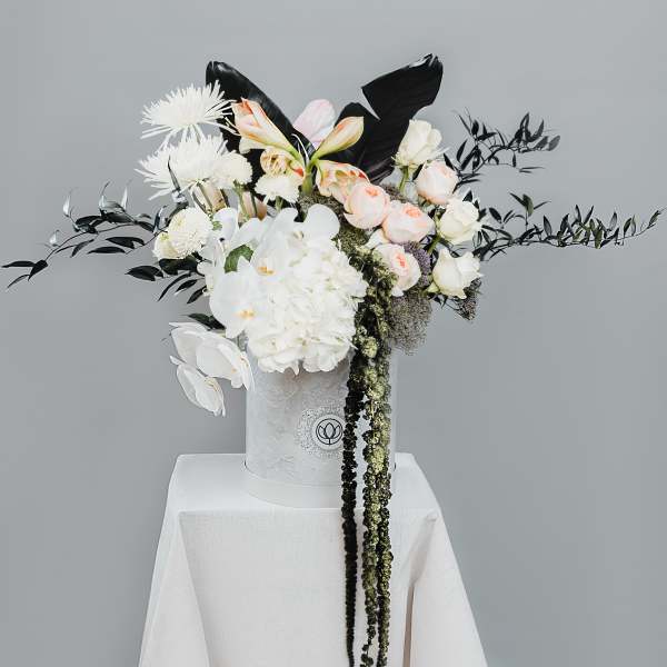 White and blush floral arrangement in a white hatbox on a draped pedestal