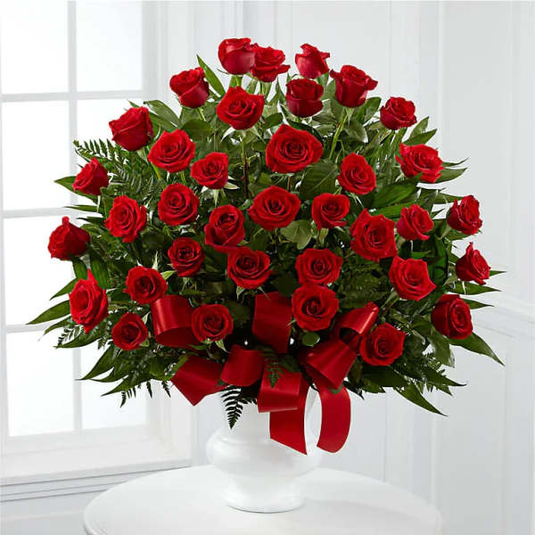 Red roses arranged in a white vase with a red ribbon