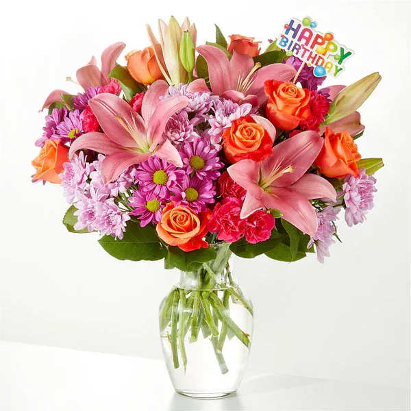 Mixed bouquet of pink lilies, roses, and daisies in a glass vase with a birthday topper