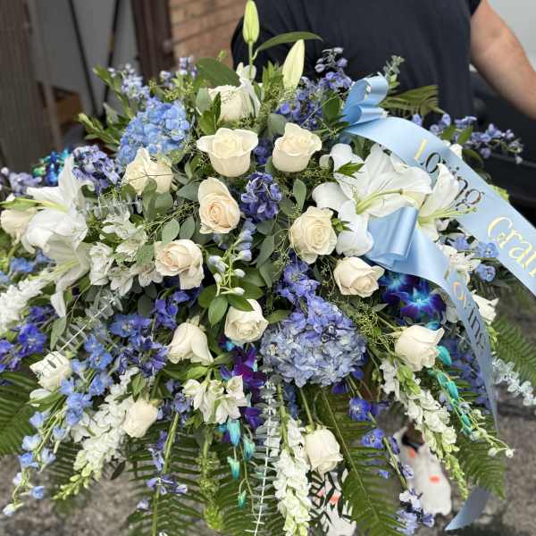 Large bouquet of white roses, lilies, and blue flowers with a ribbon