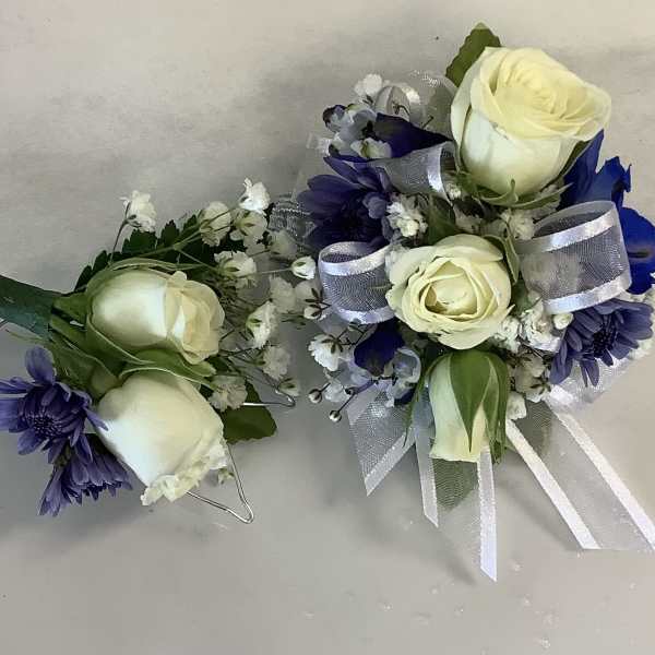 Two small floral corsages with white roses and purple flowers, tied with silver ribbon.