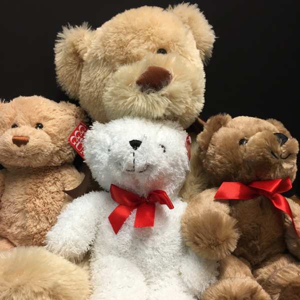 Assorted teddy bears with red bows on a wooden surface
