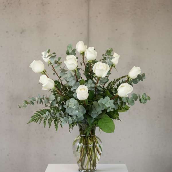 White roses arranged in a clear glass vase with eucalyptus foliage