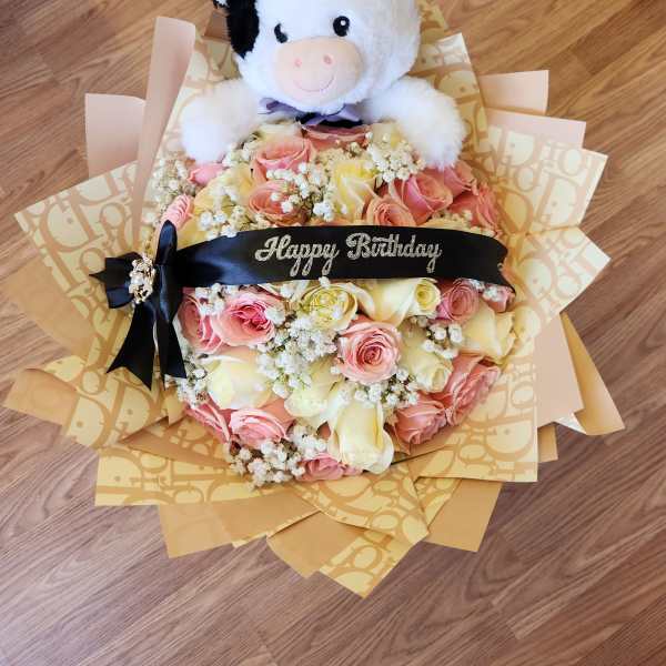 Bouquet of pink and cream roses with a plush cow topper