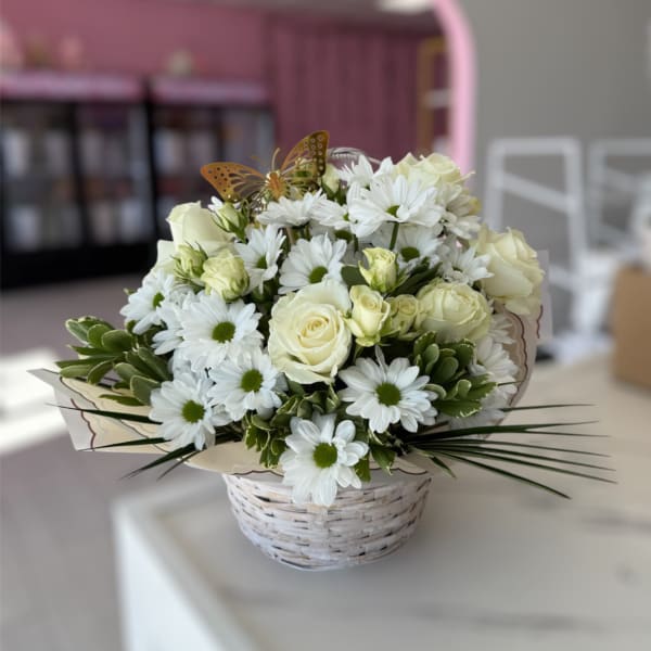 White daisies and cream roses in a white basket with a butterfly pick