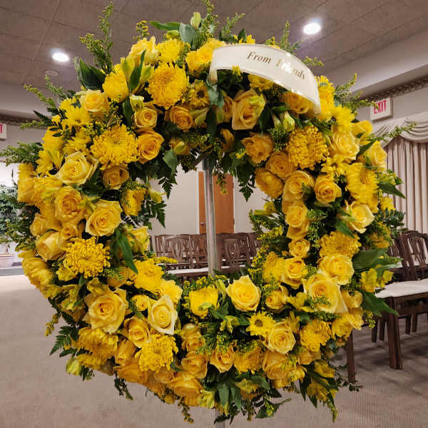 Large yellow floral wreath on a stand with a ribbon reading "From Friends"