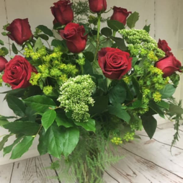Tall arrangement of red roses with green filler flowers in a clear glass vase