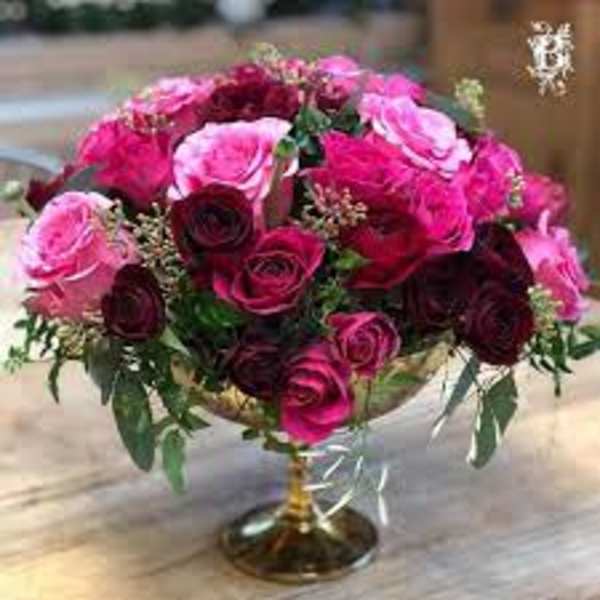 Low centerpiece of hot pink and dark red roses arranged in a gold pedestal bowl
