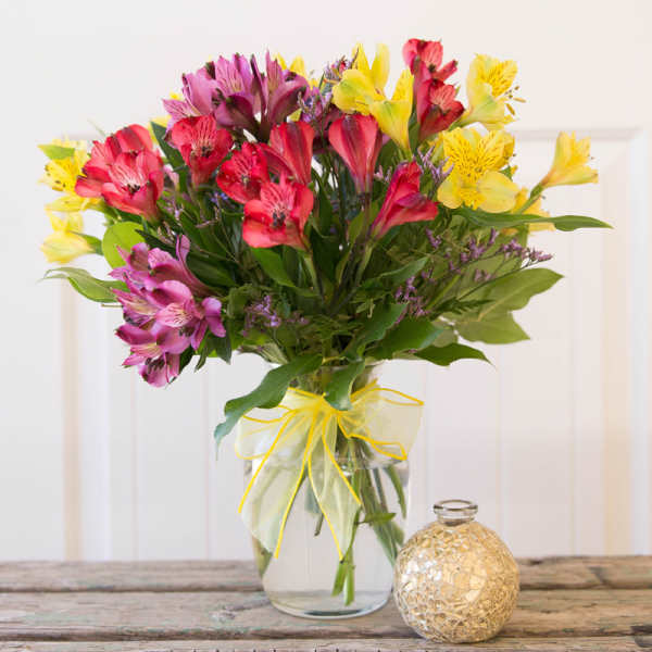 Bouquet of pink, yellow, and purple flowers in a glass vase with a ribbon