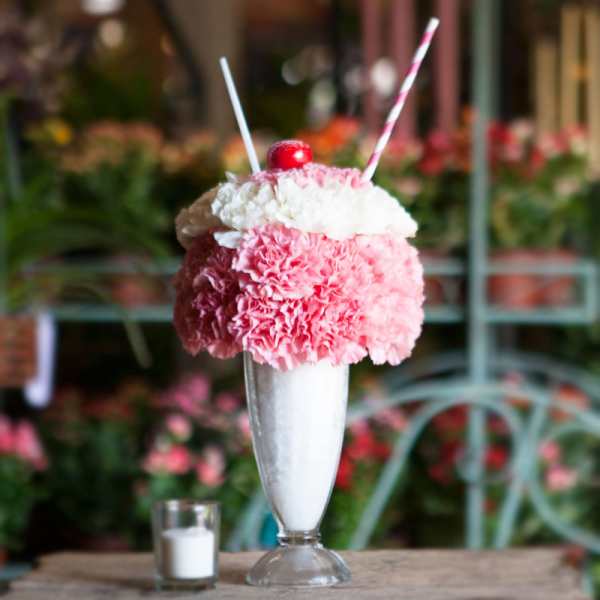 Pink and white carnations in a tall glass dessert glass with straws