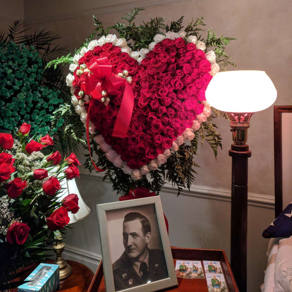Heart-shaped red rose wreath with a red ribbon beside a framed portrait