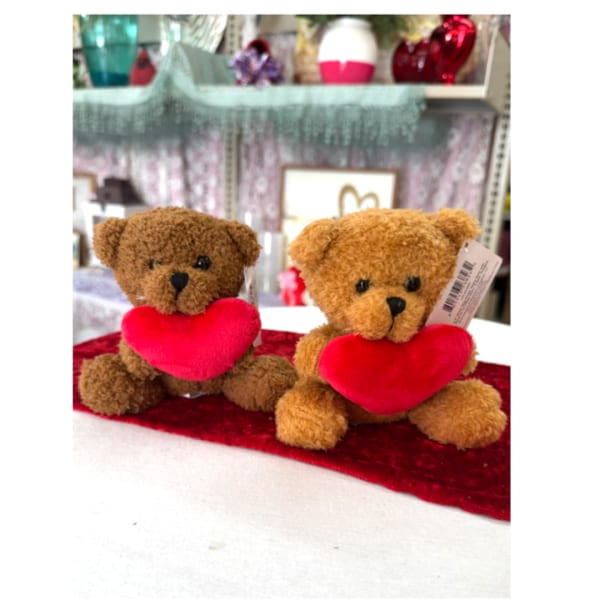 Two teddy bears holding red hearts on a red cloth