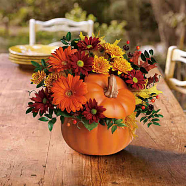 Pumpkin centerpiece with orange and red flowers on a wooden table