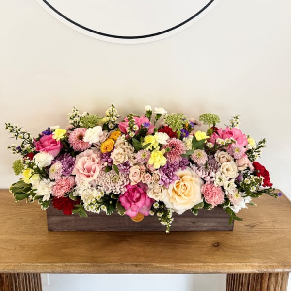 Low floral centerpiece in a rectangular wooden box with pink, white, and yellow blooms