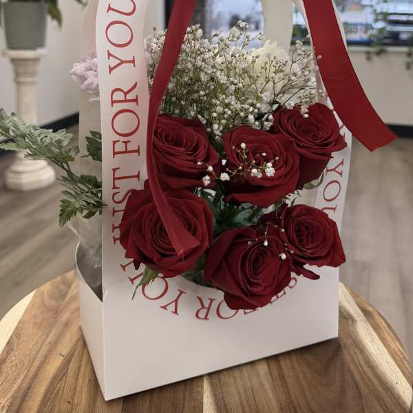 Red roses and baby's breath in a white gift bag with a red ribbon