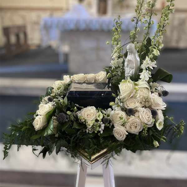 White rose funeral arrangement with a religious statue and tall white flowers