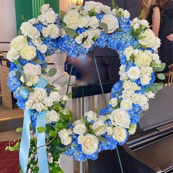 Heart-shaped floral wreath of white roses and blue hydrangeas on an easel
